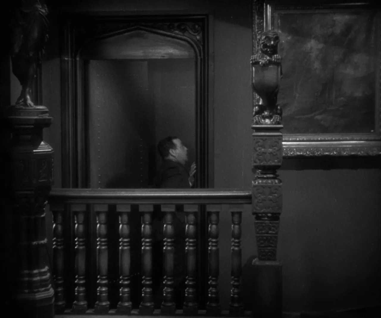 Interior balcony shot showing an ornate railing and post with a man in the doorway beyond.