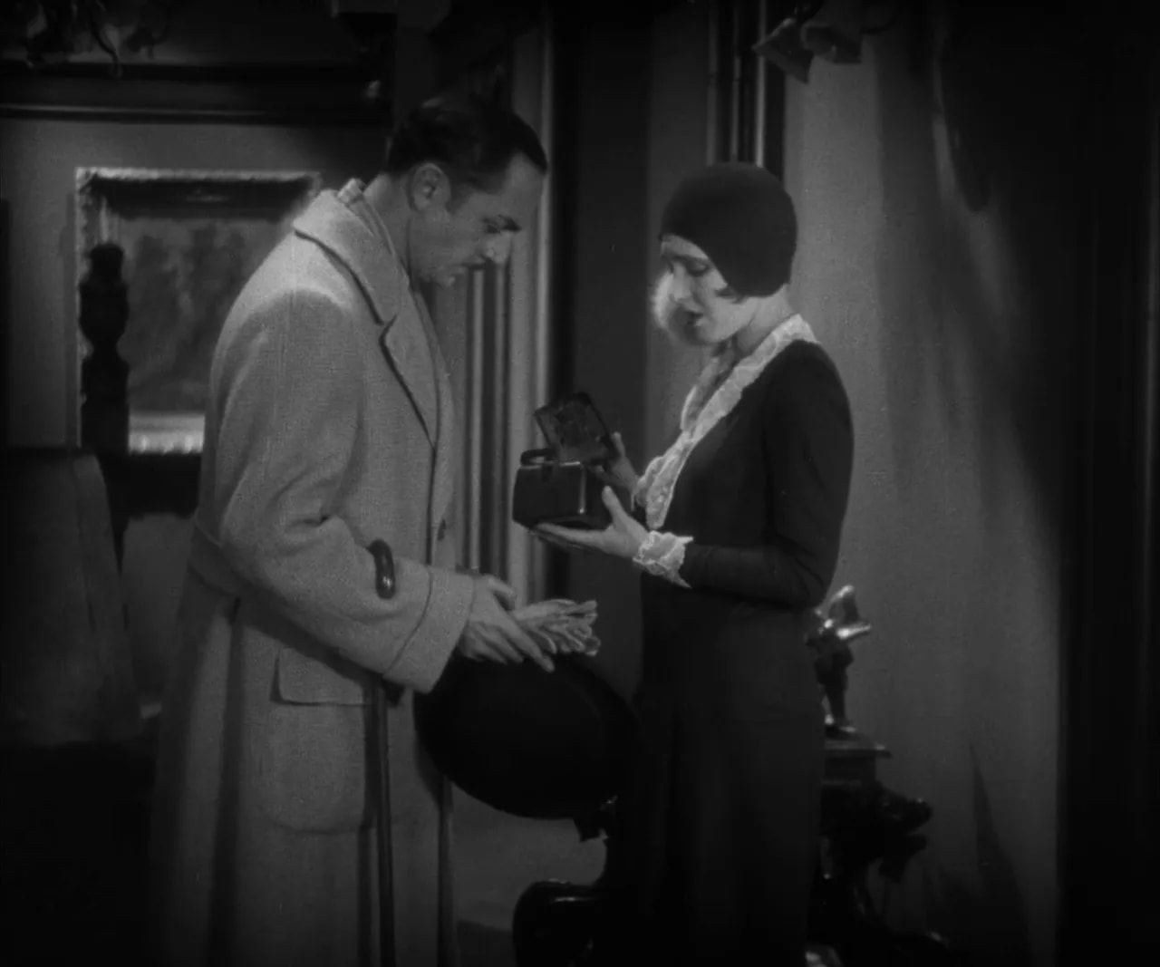 Clear black-and-white frame of The Greene Murder Case: man and woman standing face-to-face with the woman holding an open small box; the object and their expressions are visible.