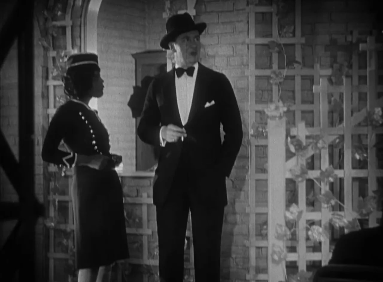 Crisp shot of Black Cat nightclub showing a man in a tux and hat beside a hostess by a trellis