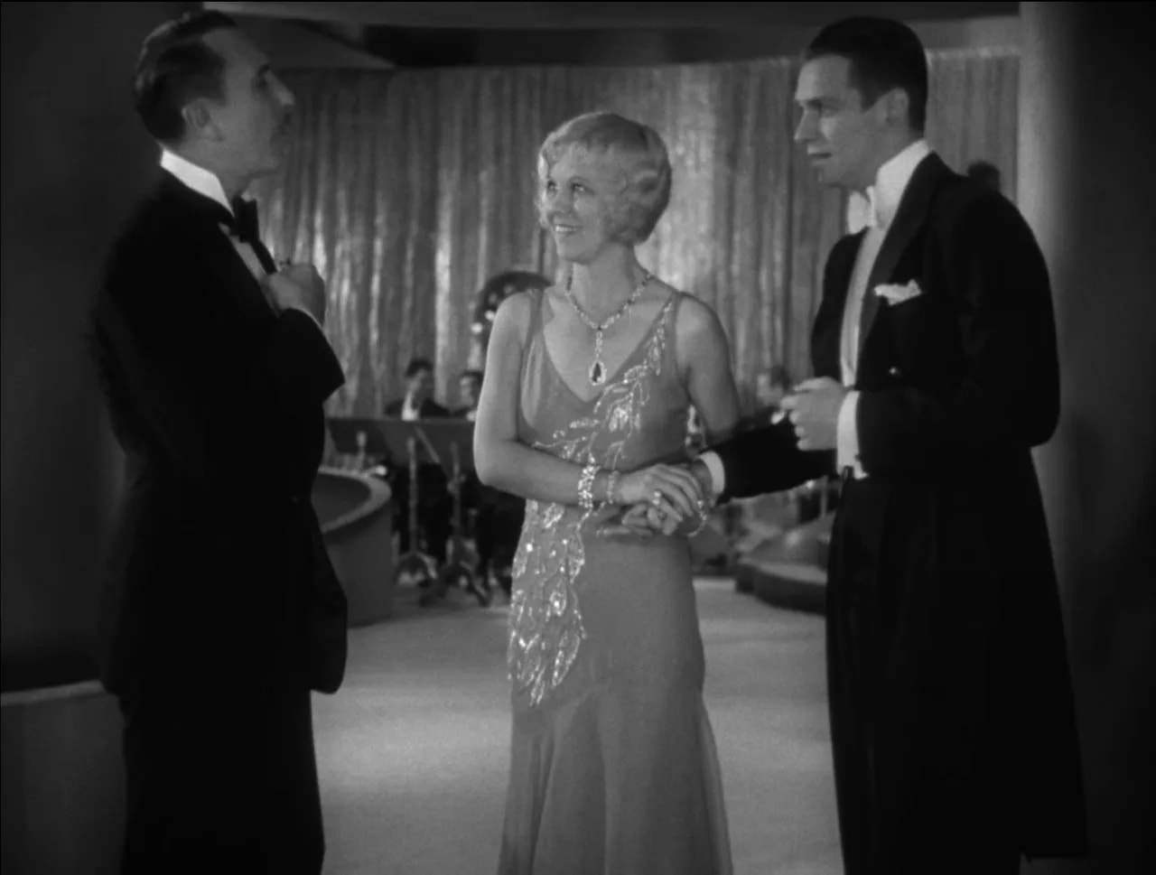 Black-and-white Little Caesar banquet scene with Olga smiling while flanked by two men