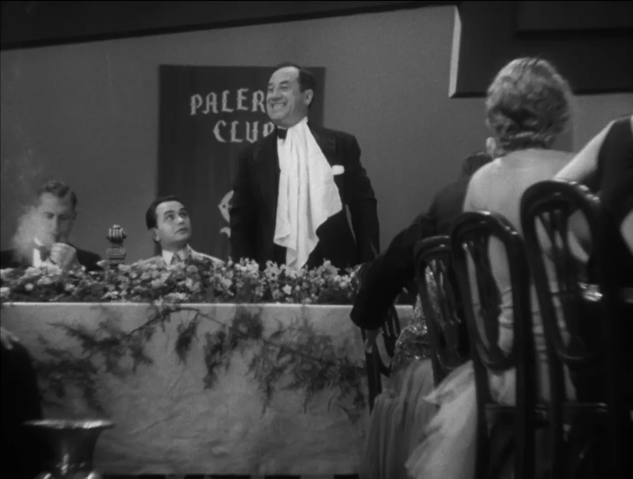 Little Caesar banquet scene with Rico speaking at the front while guests sit in a black-and-white club hall